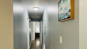 A hallway with a wooden floor, a ceiling light, and a framed picture on the wall. - 3BR Coastal Cottage | Deck + Grill (Pensacola)