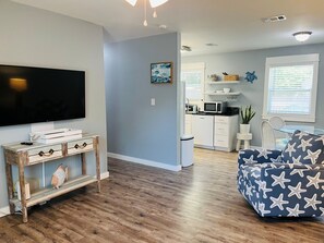 A living room with a flat-screen TV, a rustic console table, and a blue sofa with starfish pattern. - 3BR Coastal Cottage | Deck + Grill (Pensacola)