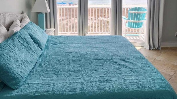 A bedroom with a large bed, a ceiling fan, and a view of the beach through the window. - Dory A: Pet-Friendly Beachfront Townhome (3BR/2BA) (Pensacola)