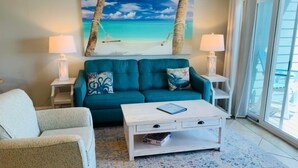 A living room with a teal sofa, a white coffee table, and a beach-themed painting on the wall. - Dory A: Pet-Friendly Beachfront Townhome (3BR/2BA) (Pensacola)
