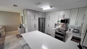 A modern kitchen with white cabinetry, stainless steel appliances, and a marble countertop.