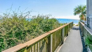 A pathway leading to a beach with a wooden railing and a building on the right.