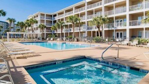 A hotel with a large pool area, multiple balconies, and palm trees.