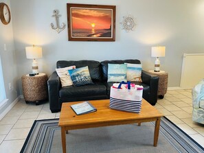 A living room with a black leather sofa, two side tables with lamps, a coffee table with a book, and decorative pillows. - Grand Caribbean 214W: Perdido Key 1BR: Ocean View, Pool, Hot Tub (Pensacola)