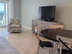 A dining area with a round table and chairs, a television on a cabinet, and a view of the ocean through a glass door. - Gulf Side Villas 1B Pet Friendly Gulf Front condo-Free Daily Activities (Pensacola)
