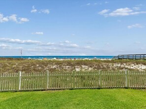 A beach view with a white fence in the foreground and a clear blue sky.