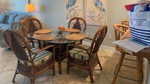 A dining area with a round glass table surrounded by wicker chairs with striped cushions. - Ocean Breeze 602W: Gulf-Front Perdido Key 2BR/2BA + Pool (Pensacola)