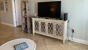 A living room with a television on a cabinet, a ladder, and a small table with a card. - Ocean Breeze 602W: Gulf-Front Perdido Key 2BR/2BA + Pool (Pensacola)