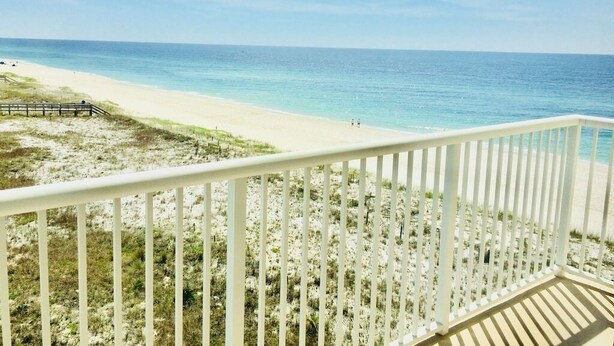 A beach view from a balcony with a white railing, sandy beach, and ocean. - SK511: Gulf-Front 3BR Corner Condo w/ Balcony (Pensacola)
