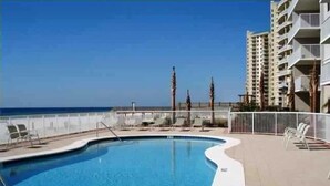 A swimming pool with a curved edge, surrounded by a white fence and lounge chairs. - SK511: Gulf-Front 3BR Corner Condo w/ Balcony (Pensacola)