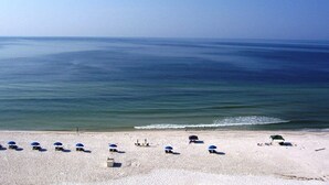 A beach with rows of beach chairs and umbrellas, a clear sky, and calm sea. - SeaSpray 1006 Gulf Front Penthouse,Pool,Tennis (Pensacola)