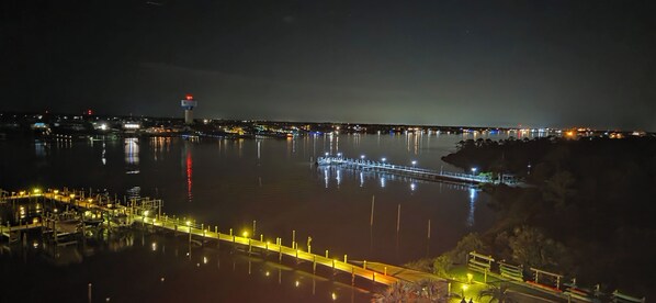 A nighttime view of a waterfront area with a dock, calm water, and distant city lights. - SeaSpray 711: 3BR/3BA + Views + Wrap Balcony (Pensacola)