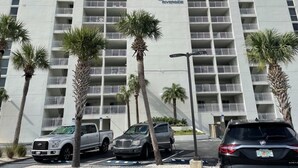Un hotel de varios pisos con balcones, palmeras y un estacionamiento.