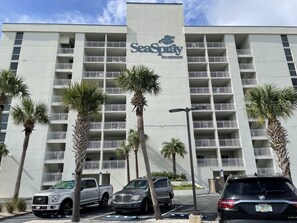 Un hotel de varios pisos con balcones, palmeras y un estacionamiento.