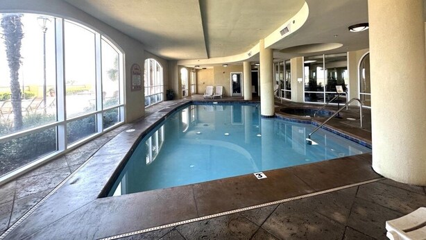 An indoor swimming pool with clear glass walls, a tiled floor, and a curved ceiling.