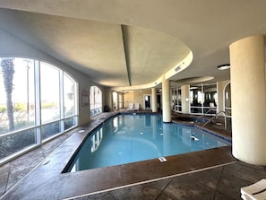 Una piscina interior con paredes de vidrio transparente, suelo de baldosas y techo curvo.