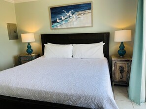 A hotel room with a large bed, two bedside tables with lamps, a painting on the wall, and a wooden cabinet with a seahorse design.