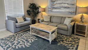 A living room with a grey sofa, a coffee table, a large abstract painting, and a potted plant.