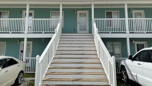A two-story building with a central staircase, white railings, and a green exterior.