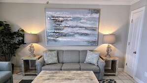 A living room with a grey sofa, two side tables with lamps, a coffee table, and a large abstract painting on the wall.