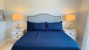 Una cama con cubrecolcha azul acolchado, dos mesitas de noche con lámparas y un ancla decorativa en cada una.