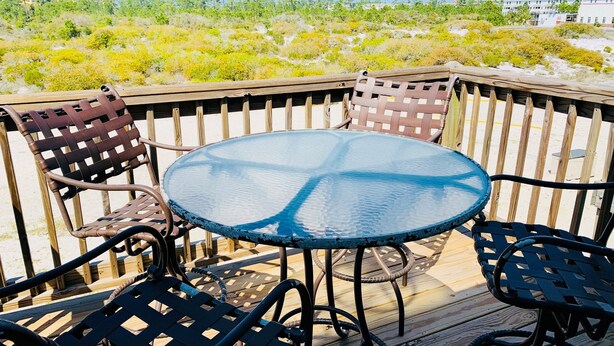 Una mesa redonda de vidrio con sillas de metal en una terraza de madera.