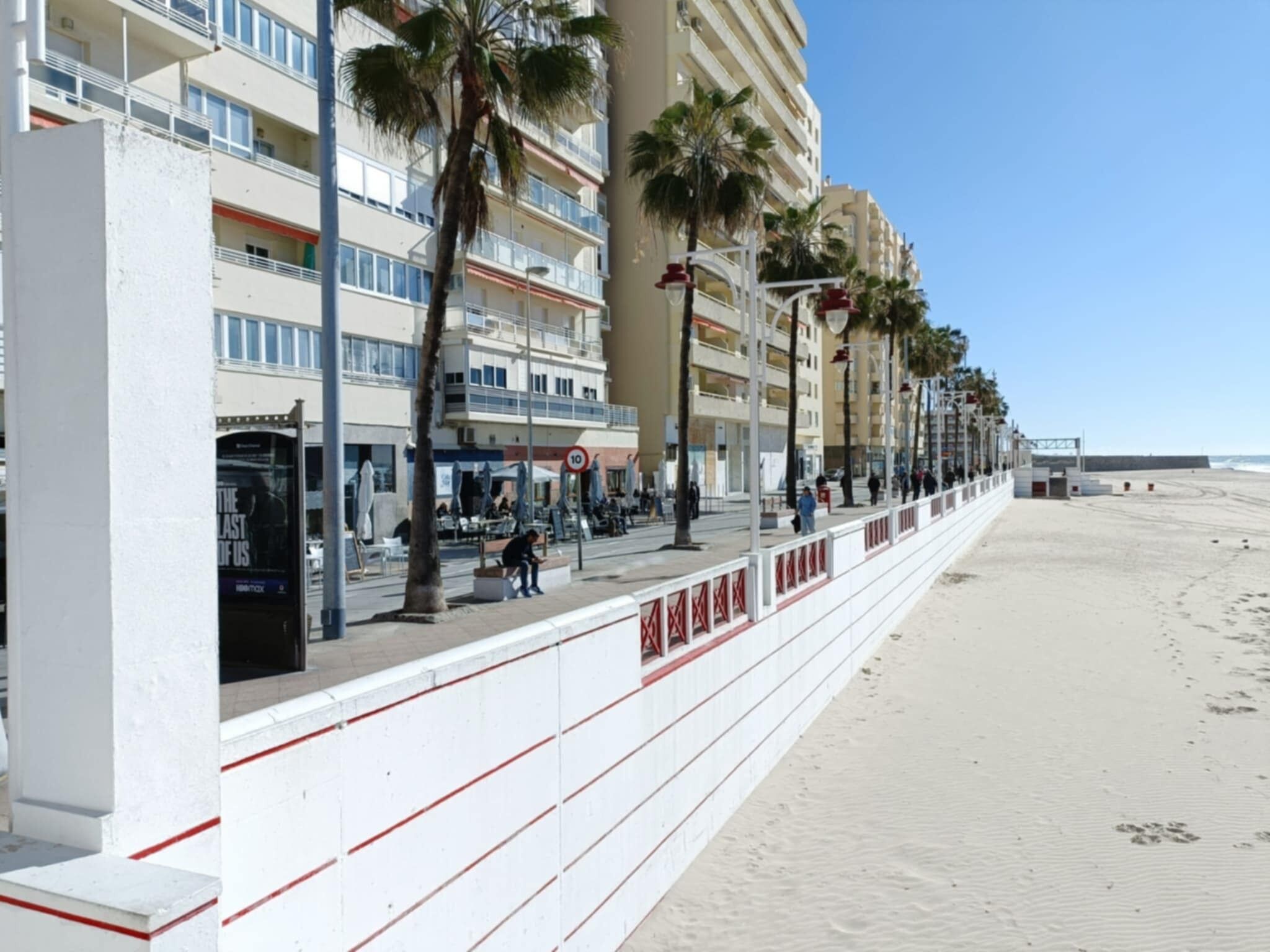 Un paseo marítimo con edificios de varios pisos, palmeras y una playa de arena.