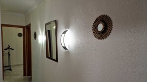 A hallway with a mirror, a wall-mounted light fixture, and a decorative sunburst mirror. - Apartamento Candari Playa (Cádiz)