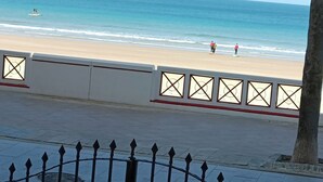 A coastal walkway with a metal fence, a beach in the background, and a clear sky. - Apartamento Candari Playa (Cádiz)