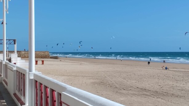 A beach with a white railing and a clear blue sky. - Apartamento Candari Playa (Cádiz)