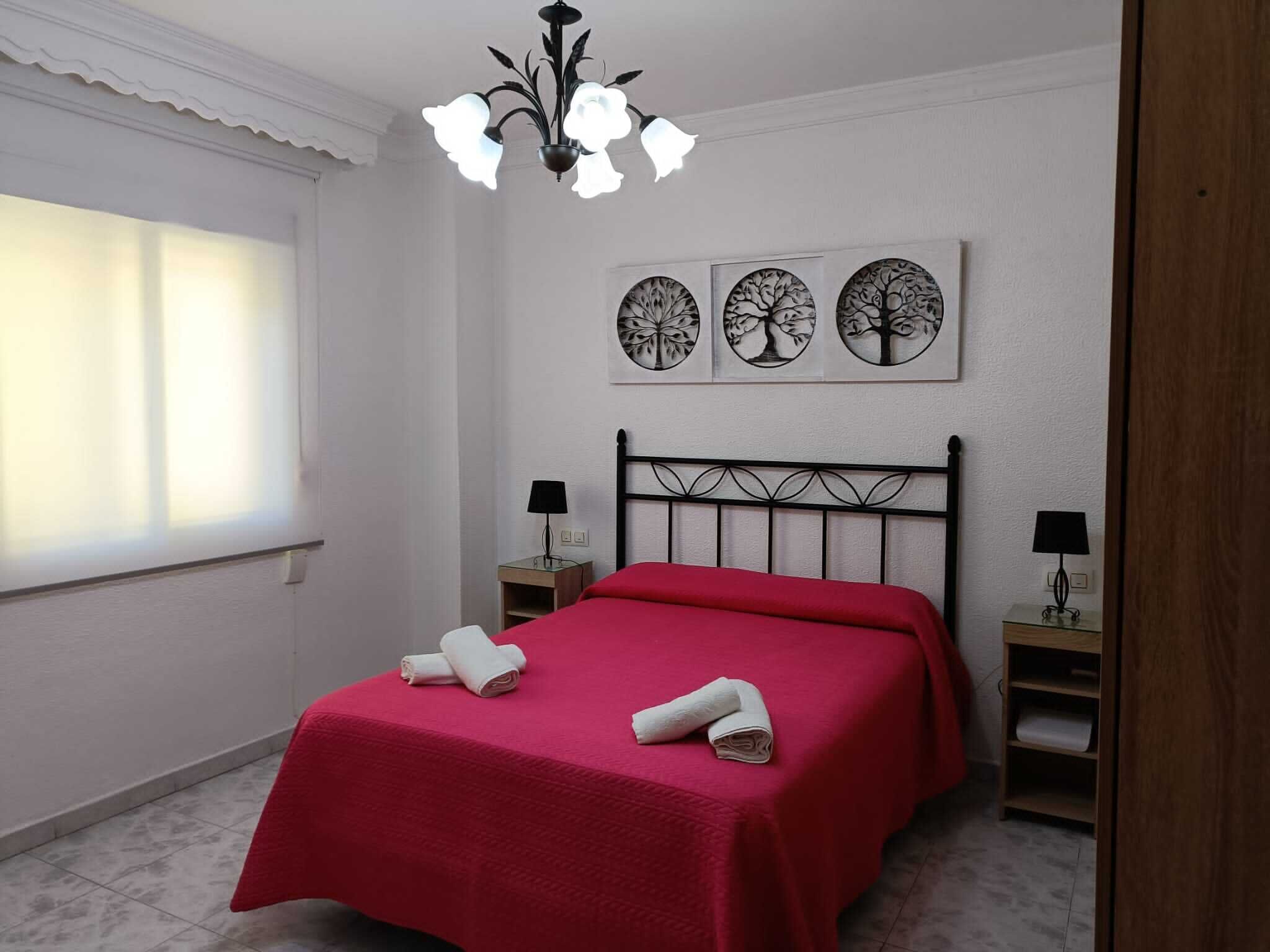 Un dormitorio con cama, dos mesitas de noche, una araña y tres obras de arte con motivos de árboles colgadas en la pared.