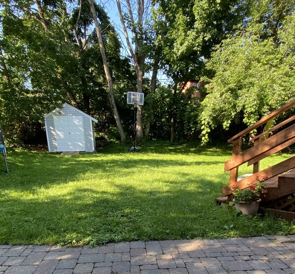 A backyard with a wooden deck, a shed, and a basketball hoop.
