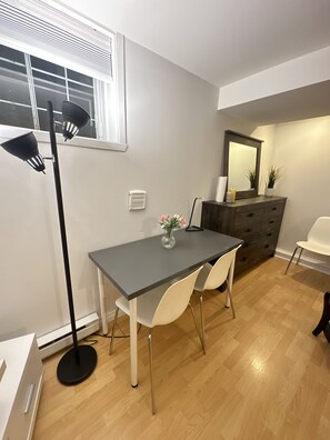 A dining area with a table, chairs, a floor lamp, a dresser, and a mirror.