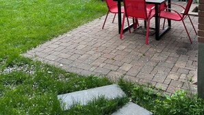 An outdoor patio with a table and chairs, a red umbrella, and a wooden deck.