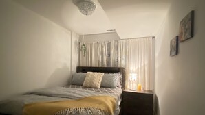 A bedroom with a bed, a nightstand, a lamp, a window with curtains, and a ceiling light fixture.