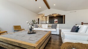 Un amplio salón con una gran mesa de centro de madera, un sofá blanco y un sillón blanco.