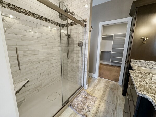 Ein modernes Badezimmer mit einer gläsernen Dusche, einem begehbaren Kleiderschrank mit Regalen und einer Arbeitsplatte aus Granit.