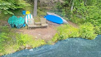 Une rive bordée de kayaks et d’un canoë, entourée de verdure.