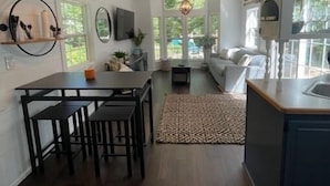 A modern kitchen with a dining area, wooden flooring, and pendant lighting. - River's Edge Tiny Home | Expansive Deck (Park Falls)