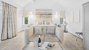 Une chambre moderne avec un grand lit, un canapé, une table de chevet avec une bouteille et des verres, et un ventilateur.