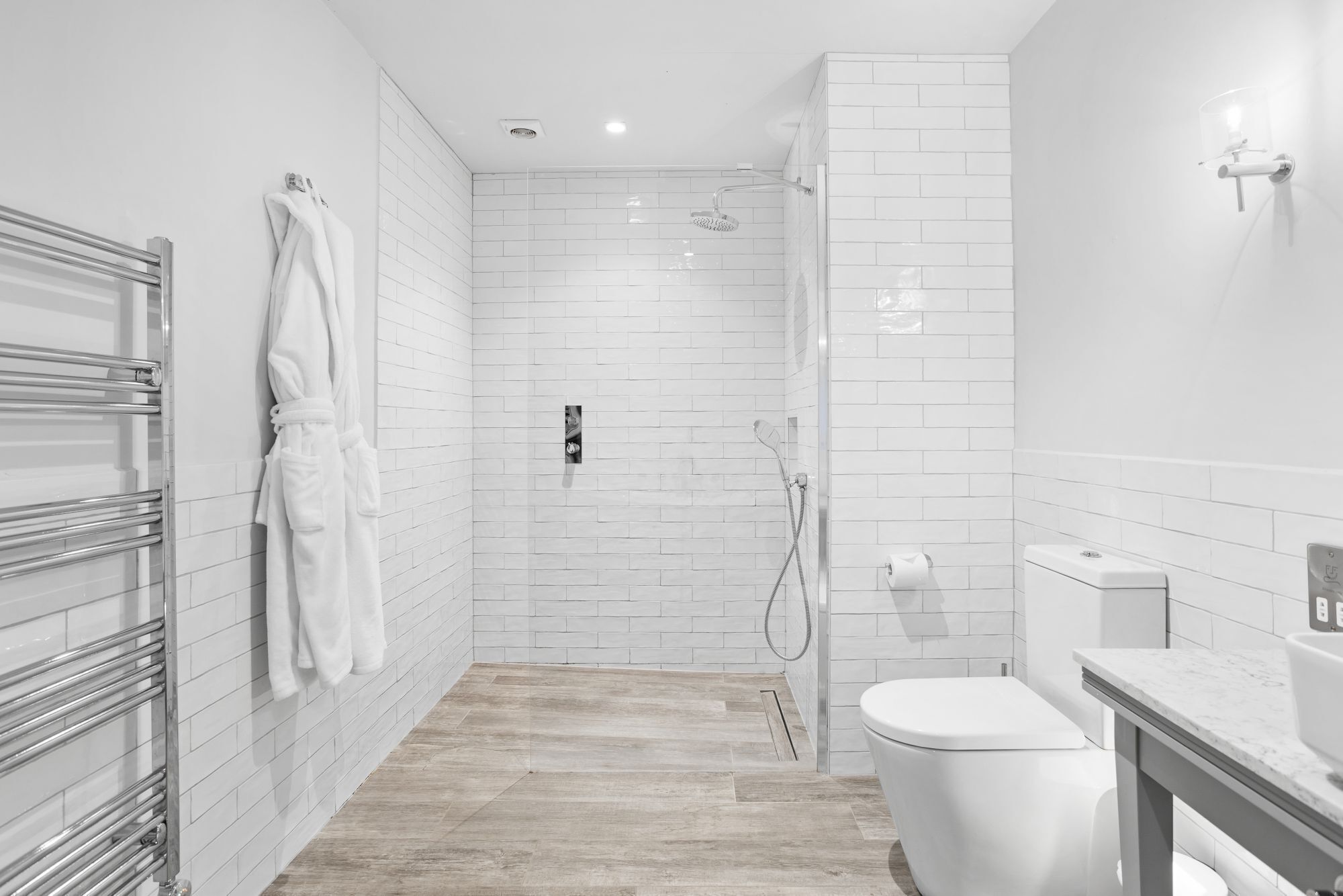Ein modernes Badezimmer mit weißen Fliesen, einer Glasdusche, einer Toilette und einem Handtuchhalter.