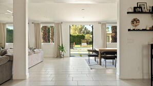 A spacious living area with a sofa, dining table, and chairs, leading to a garden view.