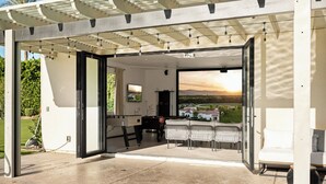 An open patio with a pool, outdoor seating, and a view of a sunset over a landscape.