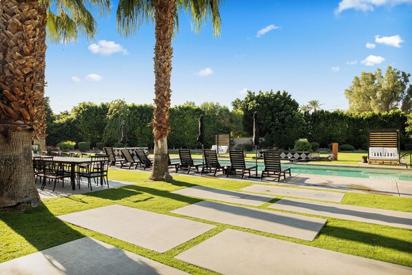 Zona junto a la piscina con sillones de descanso, una mesa de comedor y un césped cuidado.