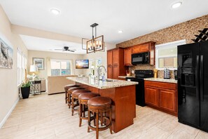 A modern kitchen with a central island, bar stools, wooden cabinets, a black refrigerator, and a microwave.