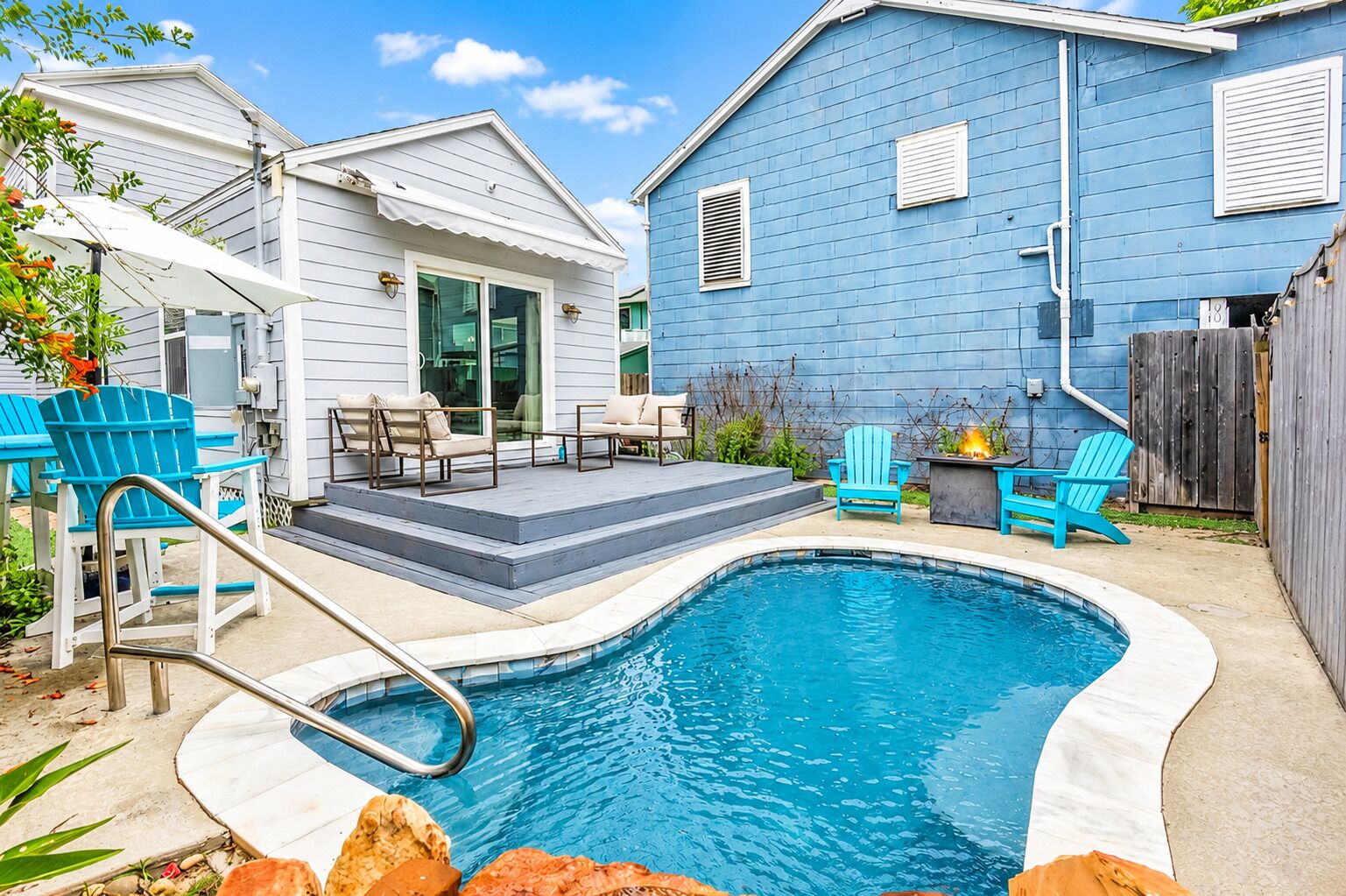 A backyard with a swimming pool, outdoor seating, and a blue house.