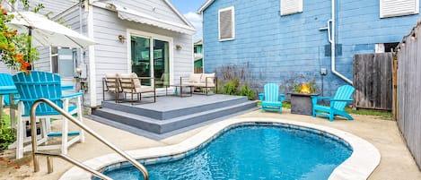 A backyard with a swimming pool, outdoor seating, and a blue house.