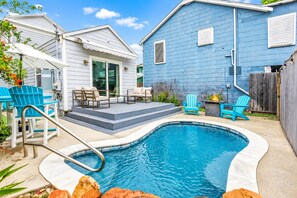 A backyard with a swimming pool, outdoor seating, and a blue house.