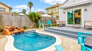 A backyard with a swimming pool, a wooden deck, and outdoor furniture. - Heated Pool | Pet Friendly | Fire Pit | Near Beach (Galveston)
