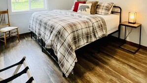 A bedroom with a bed, a bedside table with a lamp, a window with blinds, and a chair. - In-Town Home, Hot Tub, Wifi & Minutes to Skiing (Red Lodge)